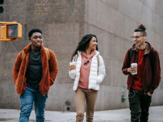 happy young multiracial friends smiling while walking on street with takeaway coffee