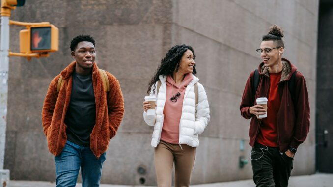 happy young multiracial friends smiling while walking on street with takeaway coffee