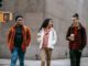happy young multiracial friends smiling while walking on street with takeaway coffee